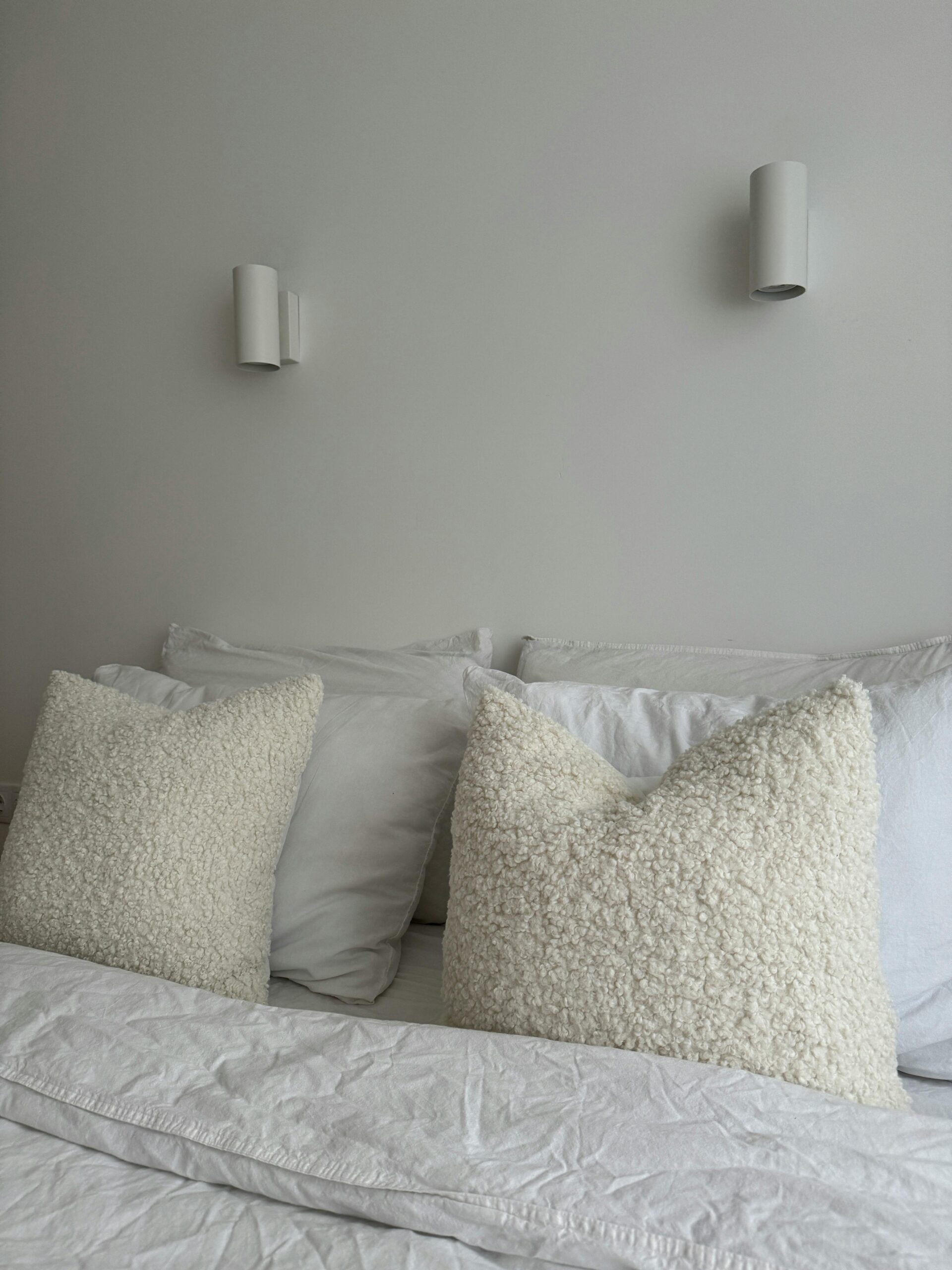 Cozy bedroom with fluffy pillows, bedside wall sconces, and warm layered light supports Thoughtful Lighting Placement to Enhance Ambiance by showing the room feature the section discusses.