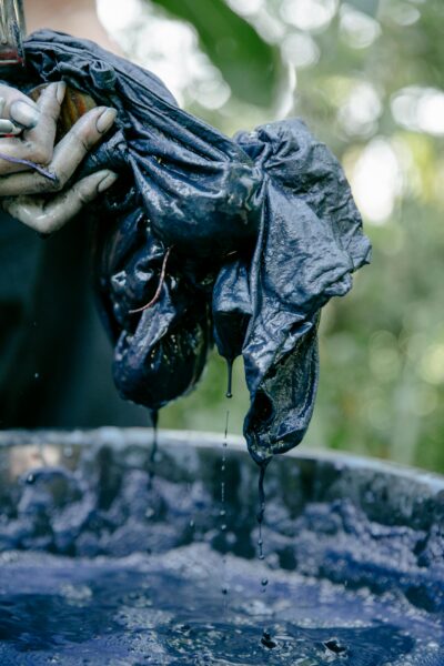Close-up of hands tie-dyeing fabric with blue dye outdoors.