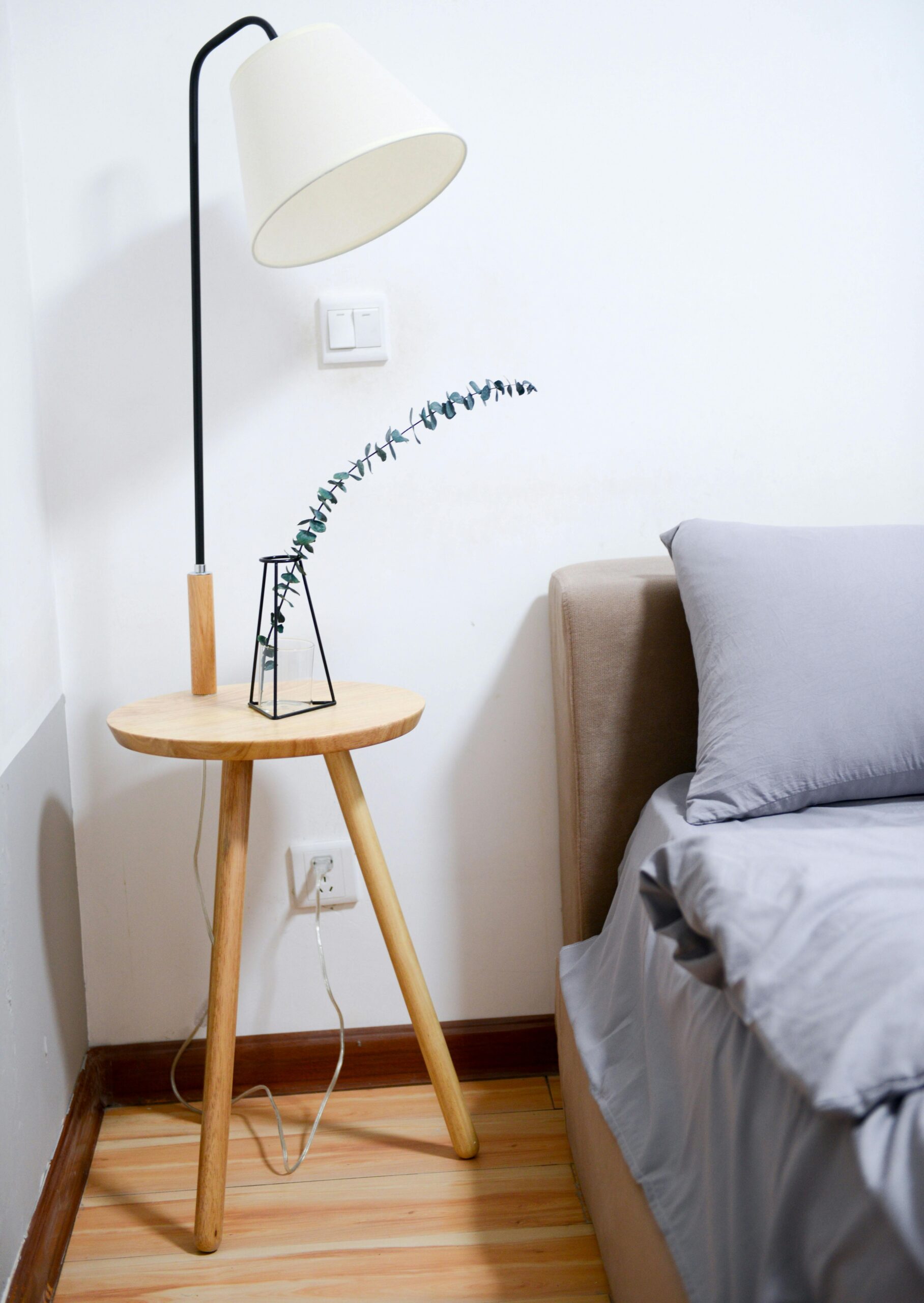 Bedroom with wooden nightstand, simple lamp, gray bedding, and natural material restraint supports Balancing Bedside Clearance for Comfort and Function by showing the room feature the section discusses.