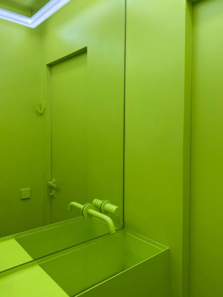 Bright neon green bathroom featuring a sleek sink and mirror reflection for modern design.