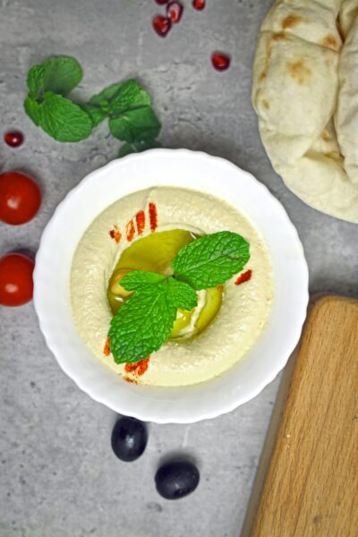 Top view of creamy hummus garnished with olive oil and mint, served with tomatoes and pita