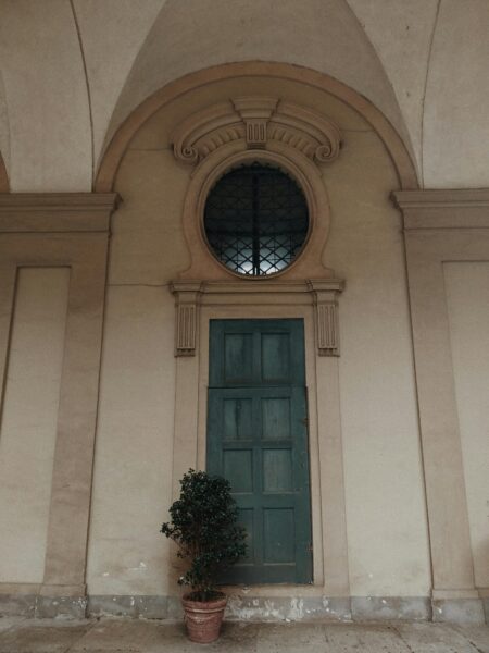 A Tuscan-style green door with ornate details set in a vintage European facade.