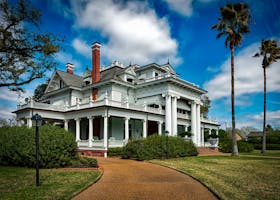 Beautiful white mansion with pillars and palm trees under a bright blue sky.