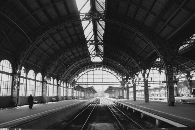 Black and white photo of an empty vintage train station interior with metal arches.