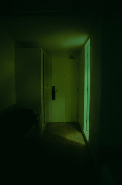 Dark hallway with a closed door, illuminated softly, creating an eerie atmosphere.