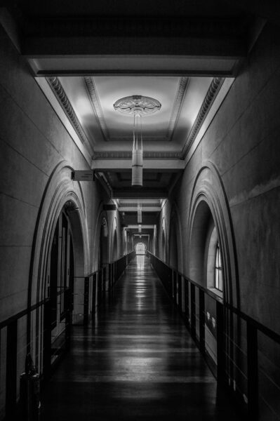 Elegant black and white photo of a long, empty arched corridor with dramatic lighting.