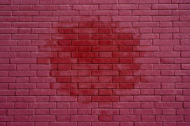 A vibrant red brick wall displaying an intriguing circular stain pattern.