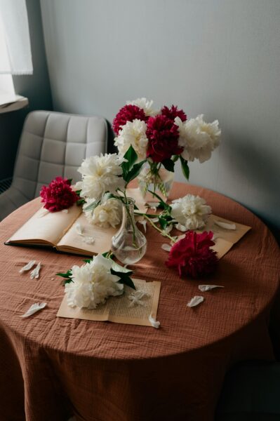 Beautiful red and white peony bouquet in a glass vase on a round table with books, creating a cozy ambiance.