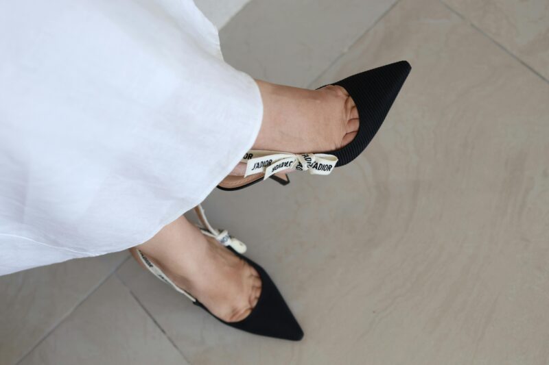 Stylish black pointed high heels paired with a white dress on tiled flooring.