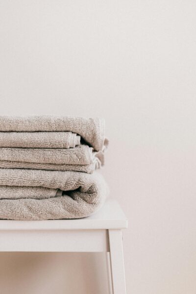 Stack of soft clean fresh gray towels placed on white minimalist stool against beige wall.