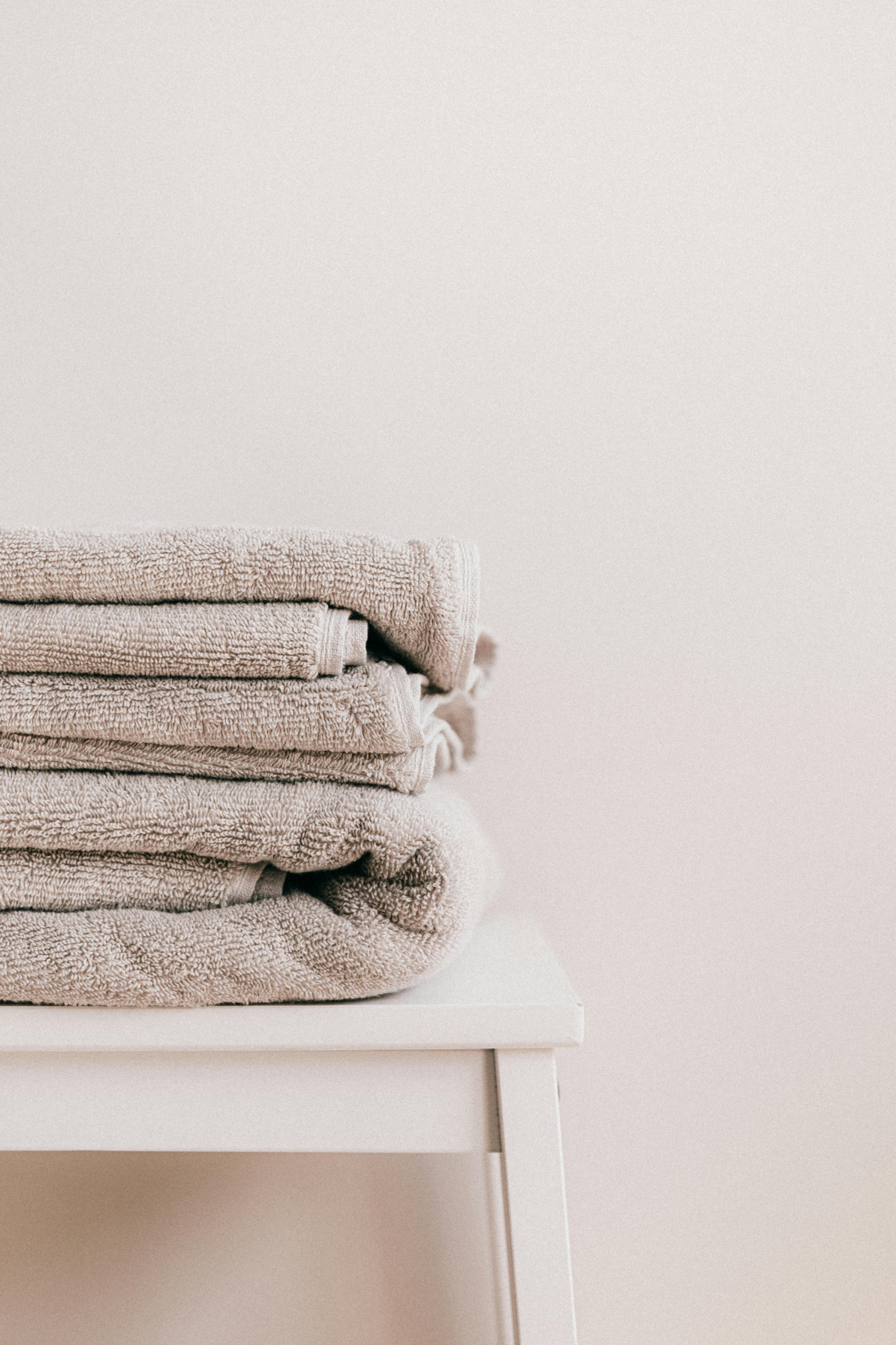 Stack of soft clean fresh gray towels placed on white minimalist stool against beige wall