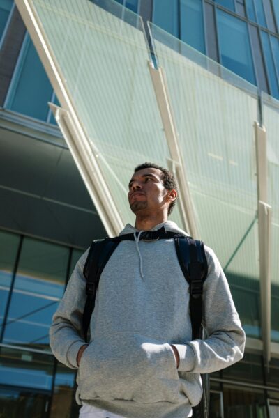 Black man with backpack in urban setting, poised for delivery near modern architecture.