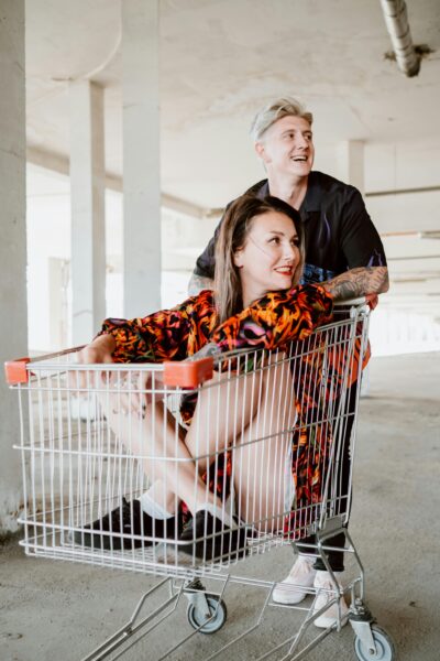 Two friends having fun with a shopping cart in an indoor parking area.