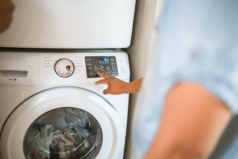Hand selecting laundry options on a digital washing machine control panel indoors