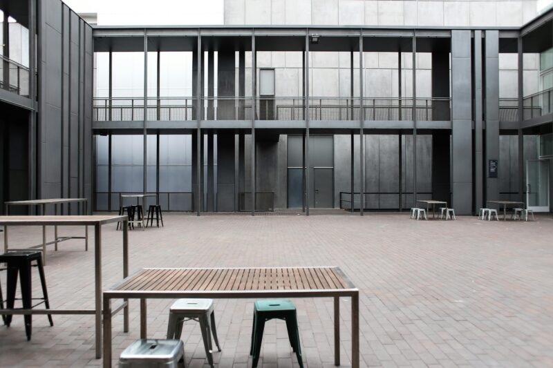 A contemporary patio space with tables and stools, surrounded by modern architecture.