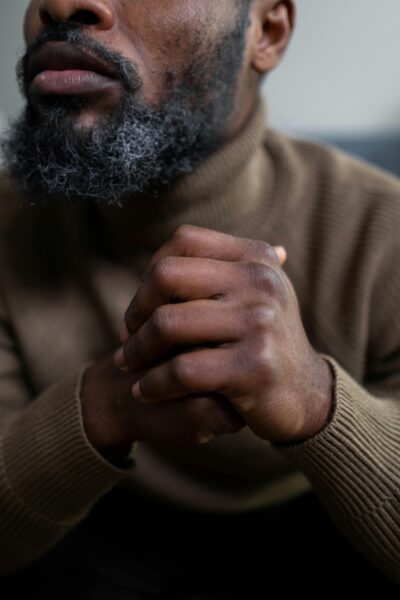 Close-up of an African man with gray beard and clasped hands, wearing a brown sweater.