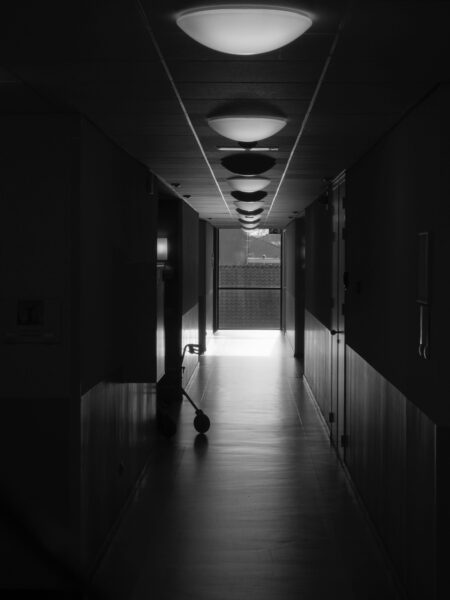 Black and white photo of a dimly lit hallway with a walker in the distance.