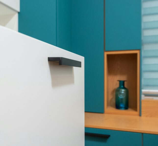 Sleek minimalist kitchen design with teal cabinets and decorative vase.