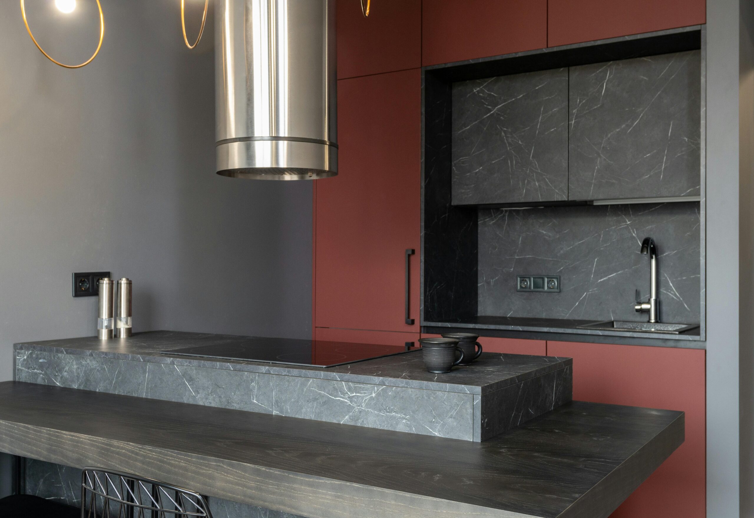 Modern interior design of small open plan kitchen furnished with cupboards and marble island counter with built in appliances and tube hood.