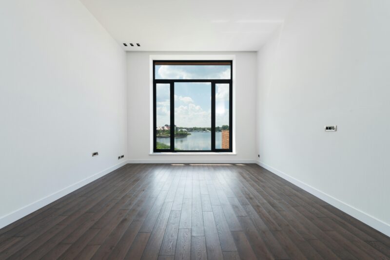 Spacious modern room with wooden laminate flooring and large windows.