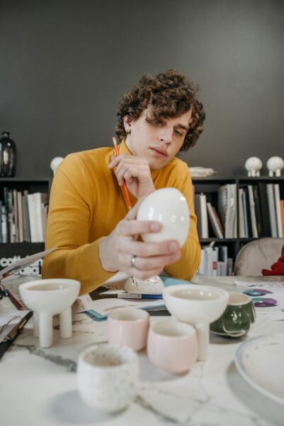 Designer examining ceramic items at a marble-topped desk with tools and plans around.