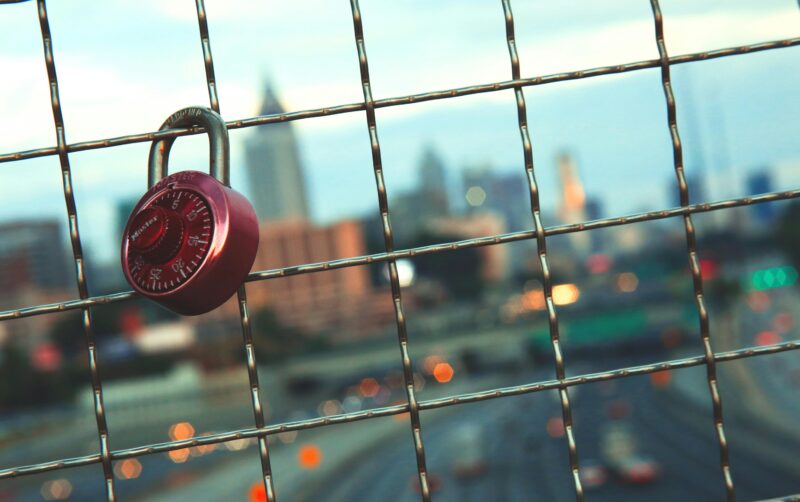 A red padlock on a wire fence with a blurred view of Atlanta's skyline during the day.