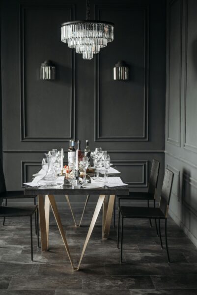 Chic dining table set with wine glasses under a stylish chandelier in a dimly lit room.