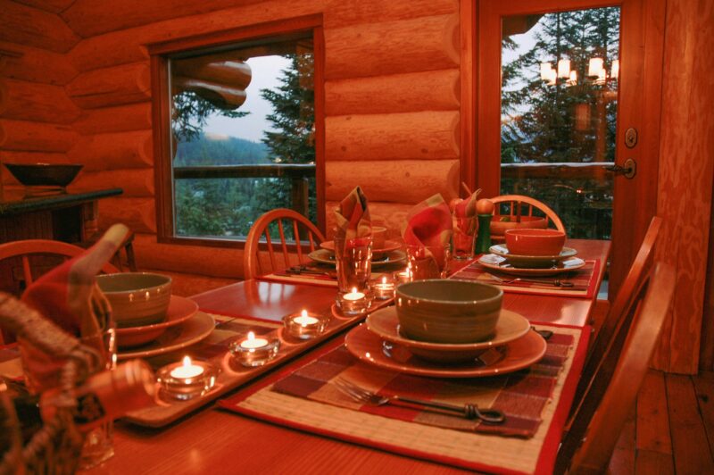 Wooden dining table with bowls and plates. Ready for dinner with candles lit, view of trees out the window.