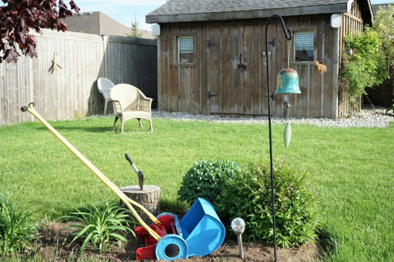 A yard with a lawn mower, garden tools and a birdhouse.