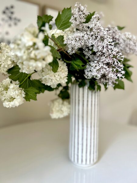 A white vase filled with lots of white flowers.