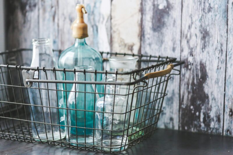 A collection of vintage glass bottles in a rustic metal wire basket on a wooden table