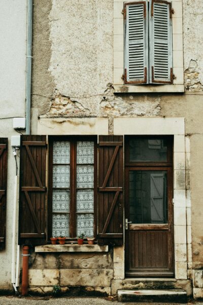 Charming rustic facade with aged wooden shutters and lace curtains, evoking a vintage French ambiance.