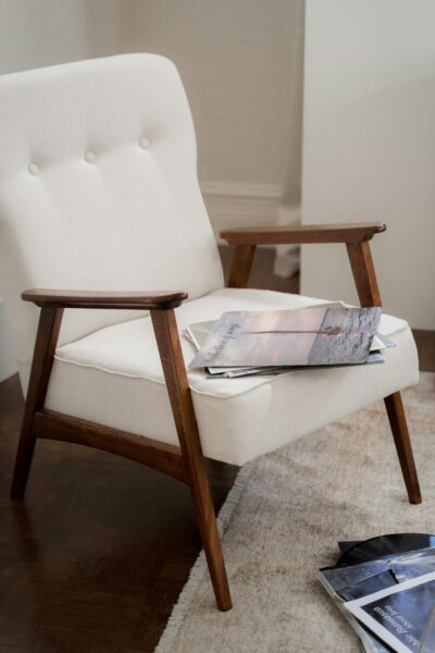 Elegant mid-century modern armchair with magazines on a plush carpet in a warm living room setting.