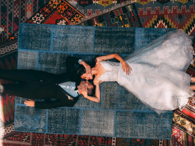 Overhead view of a newlywed couple lying on colorful carpets in Göreme, Turkey.