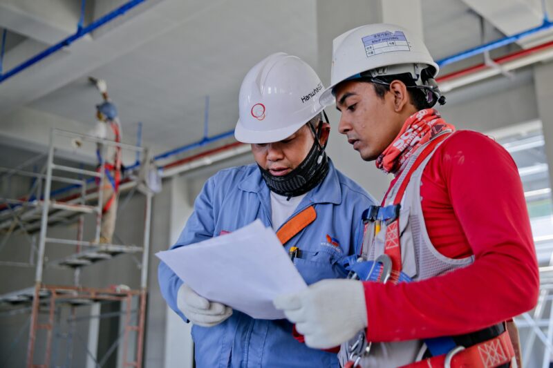 Two engineers in safety helmets reviewing construction plans at a worksite