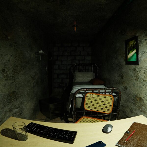 A dimly lit basement room with computer setup and a simple bed frame, creating a rustic atmosphere.