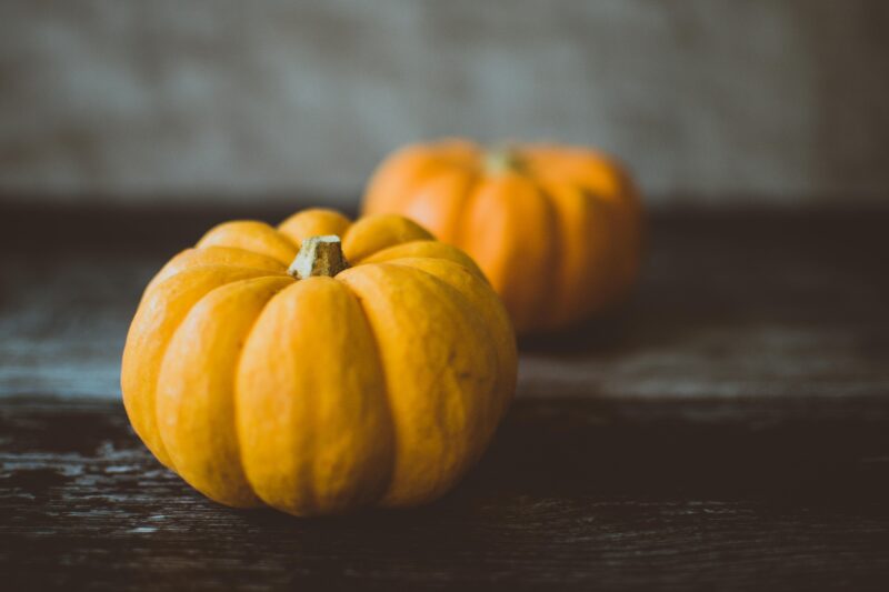 Two small orange pumpkins on a dark wooden surface, highlighting autumn vibes