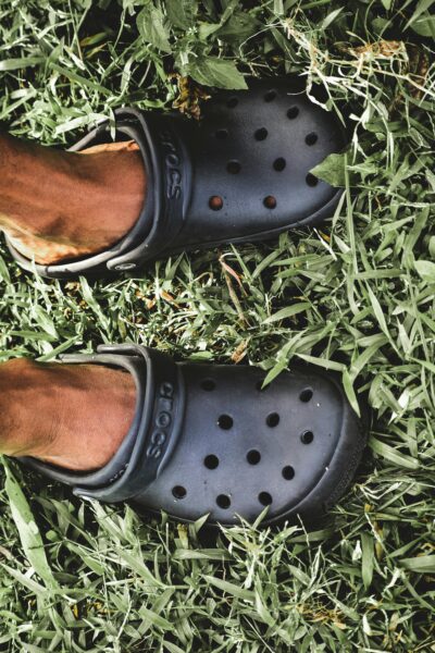 A close-up view of feet wearing black clogs standing on lush green grass.