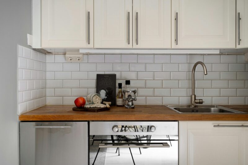 Stylish modern kitchen interior with white cabinets and wooden countertop, featuring kitchen essentials.