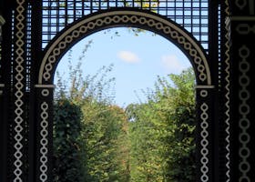 Ornate garden archway leading to a lush walkway under clear skies.