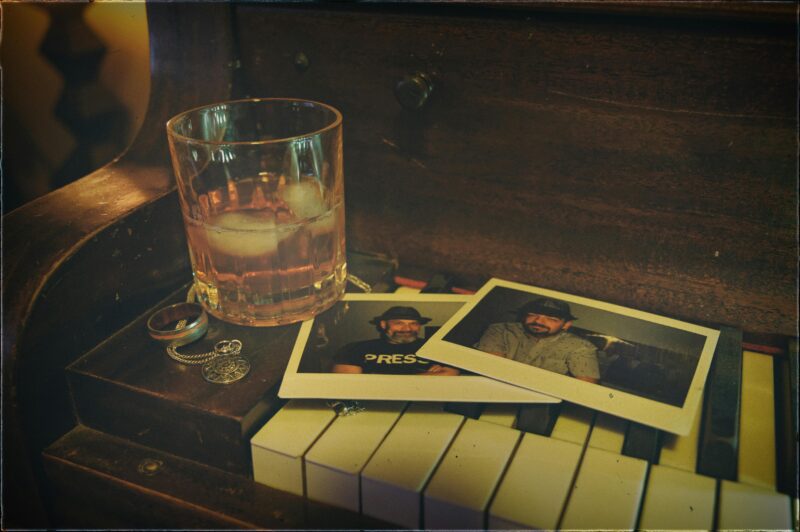 Whiskey glass with ice, vintage photos, and jewelry on a piano creates a nostalgic scene.