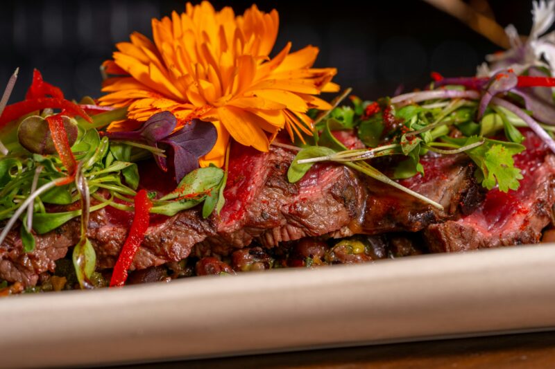 Close-up of a gourmet steak dish garnished with vibrant edible flowers and fresh greens.
