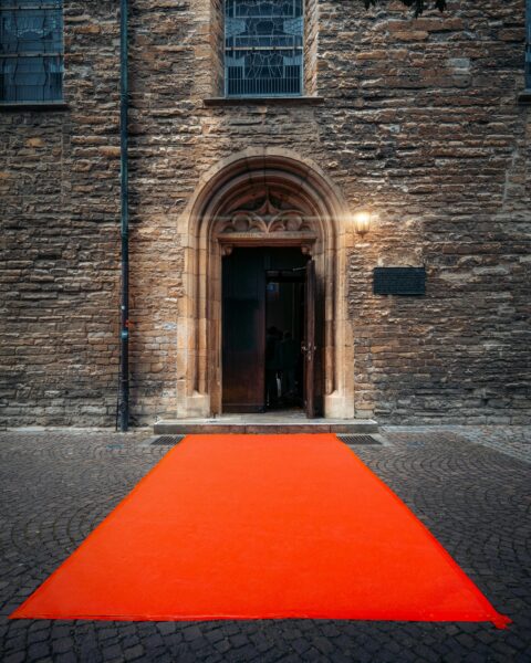 A grand entrance to a historic building featuring a vibrant red carpet leading through a stone archway.