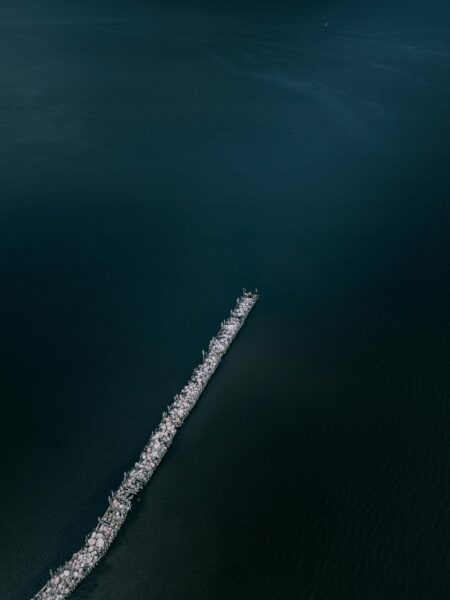 Stunning aerial shot of a long breakwater extending into calm blue-green waters