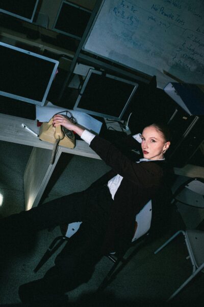 A woman in a dimly lit office interacting with a vintage telephone.