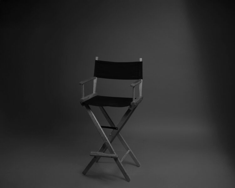 A black and white photo of a director's chair in a minimalist studio setting.