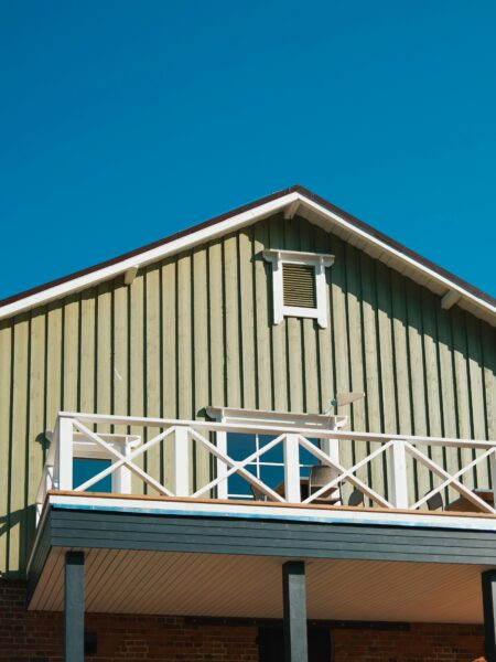 Gable of a rustic wooden house with a balcony against a clear blue sky. Architectural detail.