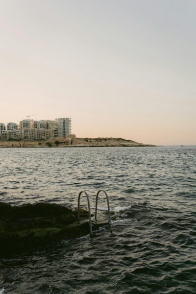 Scenic view of Malta's coastline with city skyline and tranquil sea at sunset.