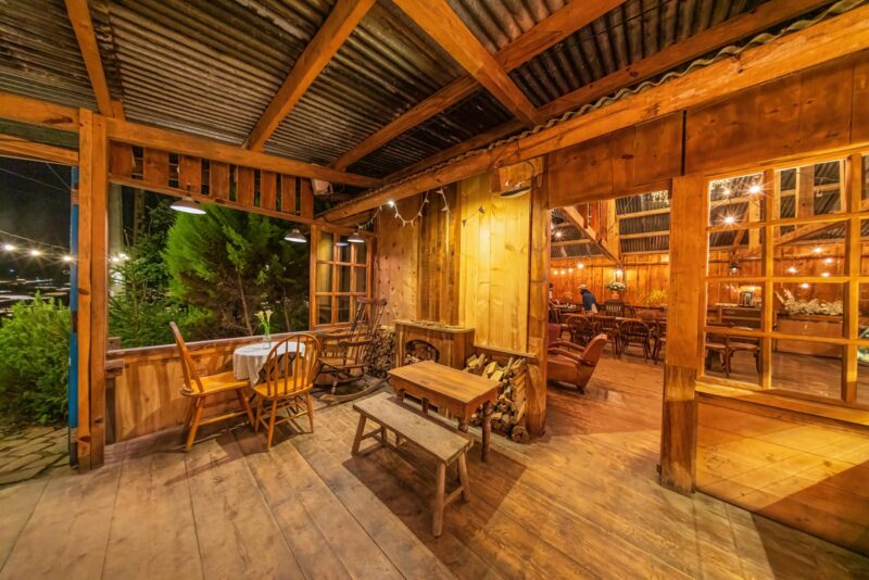 Warm, inviting rustic wooden lodge interior with glowing string lights and wooden furniture at night.