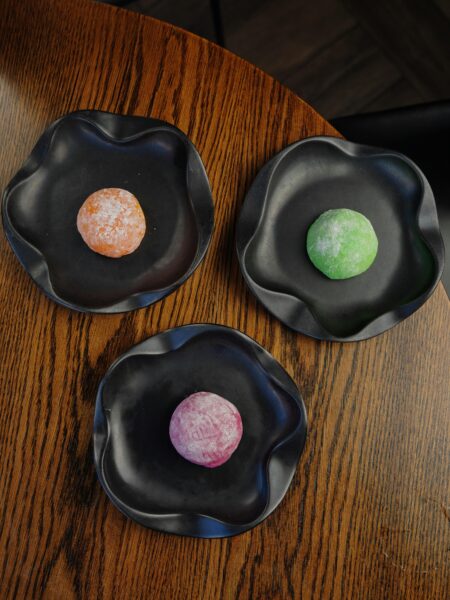 Three colorful mochi desserts elegantly displayed on black plates on a wooden table.